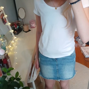 Blå jeanskjol med slitningar - Snygg blå jeanskjol med slitna detaljer och rå kant nertill. Klassisk femficksmodell med knapp och dragkedja framtill samt resår i midjan. Perfekt för dig som gillar en trendig stil.