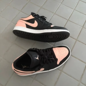 Nike Air Jordan 1 Low svart/rosa - Nike Air Jordan 1 Low Crismon Tint sneakers i svart och ljusrosa läder med vit mellansula och svart yttersula. Klassisk Jordan-logga på hälen och Swoosh på sidan. Lågt skaft och snörning framtill. Perfekt för dig som vill sticka ut med en snygg färgkombo.