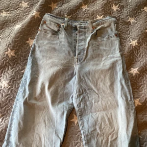 Levi's Ribcage Straight ljusblå jeans - Ljusblå Levi's Ribcage Straight jeans med klassisk femficksdesign, hög midja och raka ben. Jeansen har knäppning med flera silverfärgade knappar och den ikoniska röda Levi's-taggen på bakfickan. Perfekta för en avslappnad och trendig look. Andvända ca 10ggr