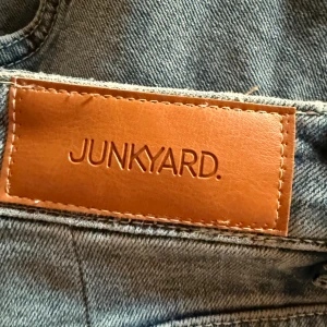 Ljusblå jeans från Junkyard - Snygga ljusblå jeans från Junkyard i boot cut. Jeansen har en normal passform och är tillverkade i mjukt denimtyg. Dem är insydda i midjan och uppsydda (jag är 165cm) men går lätt att sprätta upp alla sömmar! Därav passar Jensen både M och L!
