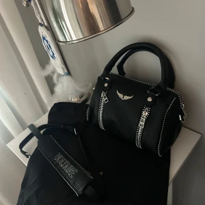 sunny bag  - Cool svart handväska från Zadig & Voltaire i grymt skinn med silverfärgade nitar och dragkedjor. Väskan har ett broderat axelband med logga och snygga metalldetaljer. Perfekt storlek för det viktigaste och ger en edgy vibe till din outfit.
