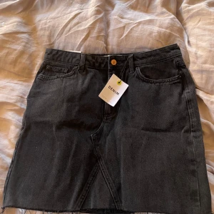 Svart jeanskjol  - Säljer en svart jeanskjol  med rå kant nertill och klassiska fem fickor. Kjolen har en snygg asymmetrisk söm framtill och är i en kort modell. 💓💓