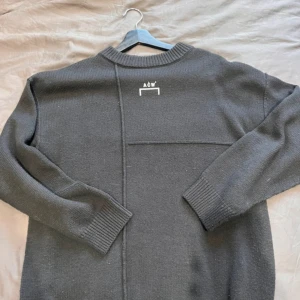 Mörkgrå stickad tröja från A-COLD-WALL* - Säljer en mörkgrå stickad tröja från A-COLD-WALL* med diskret logga i nacken. Tröjan har en unik sömdesign och ribbade muddar vid ärmslut och hals. Perfekt för dig som gillar minimalistisk och modern stil.