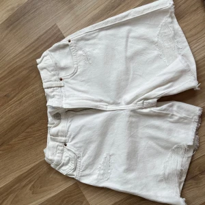 Vita jeansshorts från Zara - Säljer ett par vita jeansshorts från Zara med råa kanter och slitna detaljer. Shortsen har knapp och dragkedja framtill samt klassisk jeanslook. Perfekta för varma dagar och en avslappnad stil. Säljer eftersom att jag inte gillar hur de sitter på mig!!