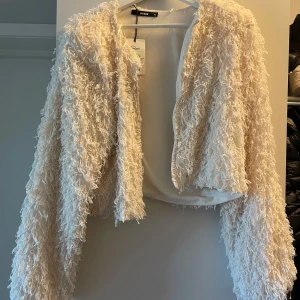 Beige/vit jacka från Bik Bok - Säljer en fluffig och trendig beige/vit jacka från Bik Bok. Jackan har långärmad design och är croppad i modellen, perfekt för att lyfta vilken outfit som helst. Den har en öppen framsida och är supermjuk med cool textur.