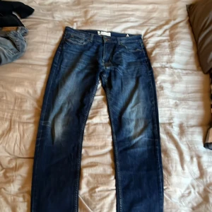 Blå jeansbyxor Dressman - Klassiska blå  jeans med raka ben och normal passform. Byxorna har fem fickor, knappgylf och tydliga slitningar för en vintage look. Perfekta för dig som gillar tidlös denimstil.