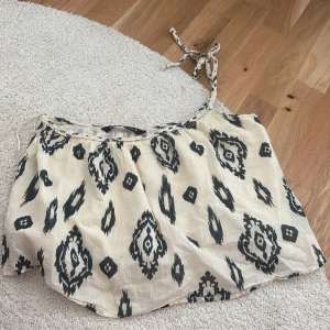Mönstrad linnetopp från Zara - Säljer en luftig och somrig linnetopp från Zara med svart och vitt mönster. Toppen har smala axelband som knyts och är perfekt för varma dagar. Materialet känns lätt och bekvämt mot huden.