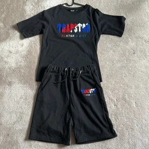 Svarta shorts och t-shirt från Trapstar med broderad logga - Säljer ett Trapstar summer sett med shorts och t shirt med broderad logga med färg blå,rött och vitt.  helt perfekt för sommaren och 500 för hela settet (300 kr st)