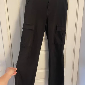 Svarta cargopants med raka ben - Säljer ett par svarta cargopants med raka ben och stora fickor på sidorna. Byxorna har normal passform och är tillverkade i ett mjukt bomullstyg. Perfekta för en avslappnad och cool stil.