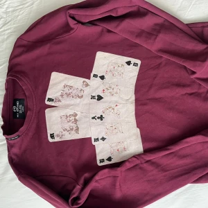 Vinröd tröja med spelkort från My Brand - Vinröd långärmad tröja från My Brand med coolt tryck av spelkort på bröstet. Tröjan har rund halsringning och är gjord i mjuk bomull, perfekt för dig som gillar unika prints och streetstyle.