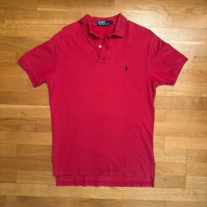 Röd pikétröja från Polo Ralph Lauren - Klassisk röd pikétröja från Polo Ralph Lauren med broderad logga på bröstet. Tröjan har krage, korta ärmar och är gjord i bomull. Perfekt för en clean och sportig look. Storleken är en amerikansk S så den passar även m bra 