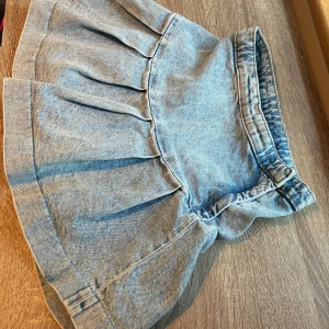Barnkjol jeans från H&M storlek 140 - Supersöt ljusblå jeanskjol från H&M med volang och veckad design. Barnkjolen har en klassisk midja och är tillverkad i mjukt denimtyg. Storlek 140. 