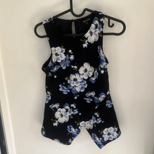 Svart blommig kort klänning från New Look - Säljer en svart kort klänning från New Look med blått och vitt blommönster. Klänningen är ärmlös och har en rund halsringning. Perfekt för dig som gillar en feminin och fräsch stil.