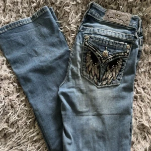 Miss Me jeans med broderade fickor - Snygga ljusblå jeans från Miss Me med broderade bakfickor och dekorativa nitar. Jeansen har raka ben och klassisk femficksdesign. Materialet är mjukt jeans med coola slitningar och detaljer som ger en unik look.