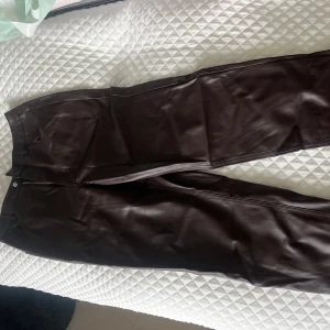 Bruna skinnbyxor  - Säljer ett par bruna skinnbyxor från Gina i storlek 38. Byxorna har normal passform, hög midja och stängs med dragkedja och knapp. Perfekta för dig som vill ha en stilren look som funkar både till fest och vardags!! Så fina och helt nya! 