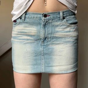 Ljusblå jeanskjol med fickor - Säljer en ljusblå, kort jeanskjol med klassiska fem fickor och snygga slitningar framtill. Kjolen har knapp och dragkedja i midjan samt dekorativa sömmar på bakfickorna. Perfekt för dig som gillar en avslappnad och trendig stil.