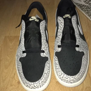 Nike Air Jordan 1 cement med elefantmönster  - Säljer ett par Nike Air Jordan cement sneakers i svart och vitt med ikoniskt elefantmönster runt tå och sidor. Skorna har vit sula, svart tåparti och klassisk Nike-logga på sidan. Perfekta för dig som gillar streetwear och unika detaljer.