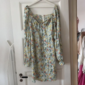 Blommig kortklänning med snörning - Supersöt kortklänning med blommigt mönster i pastelliga färger. Klänningen har långa puffärmar, snörning vid bysten och en lätt v-ringad halsringning. Perfekt för vår och sommar, med romantiska vibbar och flowy känsla.