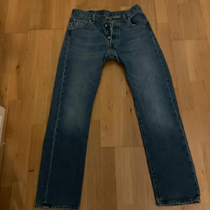Levis 501 blå jeans - Klassiska blå Levis 501 jeans med raka ben och knappgylf. Jeansen har fem fickor och en vintage tvättad look. Perfekta för dig som gillar tidlös denimstil. Storlek 30/32
