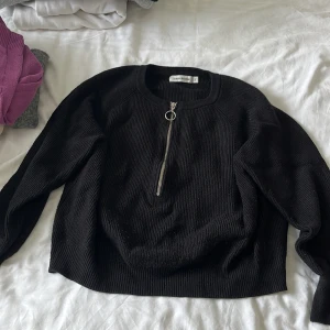 Svart stickad tröja Carin Wester S - Svart stickad tröja från Carin Wester i storlek S. Tröjan har en snygg half zip-dragkedja med ringdetalj framtill och är ribbstickad för en cool struktur. Långärmad och perfekt för lager-på-lager under höst och vinter.