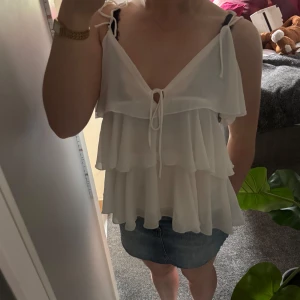Vit volangtopp med knytning 💕 - Superfint vitt linne med flera lager volanger och knytband vid axlarna samt framtill! Säljer då det inte kommer till användning. Storlek M men passar mig som brukar ha XS/S. Hör av dig för fler bilder🥰köpt på missay i Gbg 