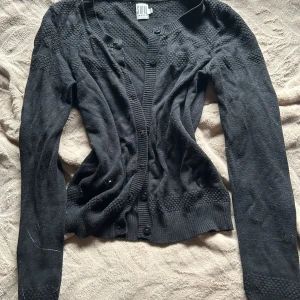 Svart kofta från Saint Tropez XS - Svart kofta från Saint Tropez i storlek XS. Den har snyggt strukturstickat mönster upptill och vid ärmslut, ribbade muddar och knäppning framtill med svarta knappar. Perfekt att slänga över en t-shirt eller linne för en chill look🖤