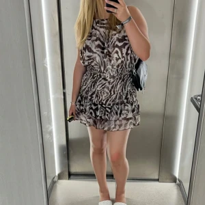 Kort klänning med zebramönster från Zara! - Säljer en snygg kort klänning med zebramönster. Klänningen har en lös passform upptill, markerad midja och volangdetalj nertill.