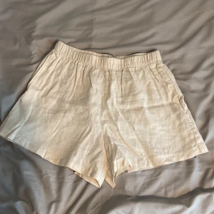 Beiga linneshorts från H&M - Snygga och luftiga beiga shorts från H&M i 100% linne. De har elastisk midja och en avslappnad passform, perfekta för varma dagar. Enkla att matcha med olika toppar för en stilren look.