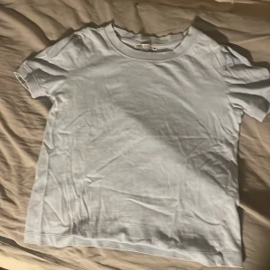 Ljusblå basic t-shirt - En enkel ljusblå t-shirt med rund hals och korta ärmar. Perfekt att matcha med jeans eller shorts för en clean och stilren look. Gjord i mjukt bomullsmaterial som känns skönt mot huden.