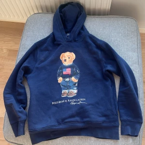 Ralph lauren hoodie - Mörkblå hoodie från Ralph Lauren med den ikoniska Polo Bear-trycket på framsidan. Tröjan har huva och långa ärmar, samt ribbade muddar vid ärmslut och nederkant. Perfekt för en avslappnad och stilren look. Pris kan diskuteras