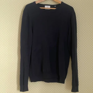 Mörkblå stickad tröja från Black - En stilren mörkblå stickad tröja från Black med rund halsringning och långa ärmar. Perfekt för lager-på-lager och enkel att matcha med olika outfits. Klassisk modell med ribbade muddar vid ärmslut och nederkant.