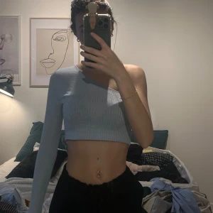 Ljusblå oneshoulder topp - Snygg ljusblå oneshoulder topp med ribbad textur. Den är croppad och har en lång ärm på ena sidan.