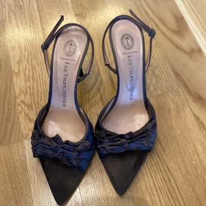 Chokladbruna klackskor från Les Tropeziennes - Eleganta chokladbruna klackskor från Les Tropeziennes med spetsig tå och smala remmar.   och en smal klack som ger en stilren look. Perfekta för en kväll ute eller en speciell tillställning.