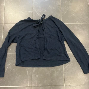 Mörkblå kofta med knytband - Säljer en stilren mörkblå kofta med knytband vid halsen. Koftan har långa ärmar och är tillverkad i ett mjukt material som ger en bekväm passform. Perfekt för lager-på-lager under kyligare dagar.