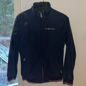 Blå vindjacka från Sail Racing - Skicka prisförslag! Säljer en snygg blå vindjacka från Sail Racing. Jackan har dragkedja framtill och två praktiska fickor med dragkedjor. Den har en stilren design med Sail Racing-logga på bröstet och en liten detalj på ryggen. Perfekt för blåsiga dagar! Tar emot byten. Nypris ca 2000