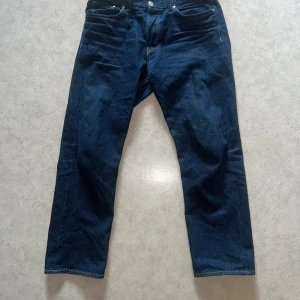 Mörkblå jeans från H&M - Snygga mörkblå jeans från H&M med klassisk relaxed fit och knappgylf. Perfekta för en avslappnad stil. Passar bra till både t-shirt och skjorta. Stolen 34/32