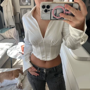 Vit satin topp med korsett  - Säljer min vita korsett skjorta från Gina Tricot då den inte kommer till användning. Finns en knapp vid handlederna så man kan välja om man vill ha armen öppen eller stängd. (På bilden är ena armen uppen och ena stängd) Storleken passar både s/m 