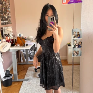 Svart glittrig klänning från Jeane Blush - Säljer en svart glittrig klänning från Jeane Blush. Klänningen har en v-ringad design och är ärmlös, perfekt för festliga tillfällen. Den har en dragkedja i ryggen för enkel påklädning.