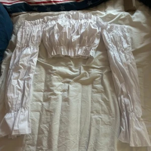 Vit offshoulder blus - Säljer en söt vit offshoulder blus med långa ärmar och elastiska detaljer. Perfekt för en somrig look eller en avslappnad dag ute. Blusen har en luftig passform och är lätt att matcha med olika outfits.