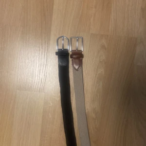 Två bälten i olika färger - Säljer två stilrena bälten, ett i svart och ett i beige. Båda har silverfärgade spännen och detaljer i skinn. Perfekta för att komplettera din outfit. 150 kr styck båda för 250