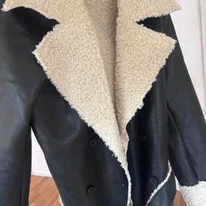 Svart skinnjacka med foder - Snygg svart skinnjacka med mjukt beige foder. Jackan har en klassisk design med bred krage och dubbla knapprader. Perfekt för kyligare dagar och ger en cool look.