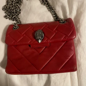 Röd quiltad axelväska från Kurt Geiger - Snygg röd axelväska från Kurt Geiger i skinn med quiltad design och en unik metallspänne framtill. Den har små defekter, men inget som syns när man bär den! Säljer då den inte kommer till användning länge! Priset kan diskuteras!
