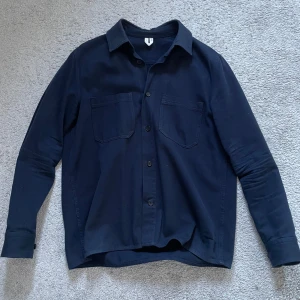 Overshirt  - Snygg marinblå  overshirt med klassisk krage och knappar framtill. Overshirten har två bröstfickor och en stilren design som passar perfekt för olika tillfällen.
