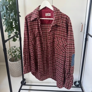 Rutig skjorta från Stockhult - Säljer en snygg rutig skjorta i rött och vitt från Stockhult. Skjortan har långa ärmar och en klassisk krage. Den är försedd med knappar framtill och har en cool detalj med jeans armbågslappar. Perfekt för en avslappnad stil!