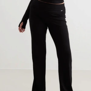 Black Eased Ribbed Pants Aimn - Snygga svarta ribbade byxor från Aimn med hög midja och en bekväm passform. Byxorna har en stilren design och är perfekta för en avslappnad look. De är tillverkade i ett mjukt och stretchigt material som ger en skön känsla hela dagen.