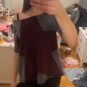 Grå och vinröd offshoulder tröja - Säljer en unik offshoulder tröja i grått och vinrött med asymmetriskt mönster. Perfekt för en avslappnad stil med en twist. Tröjan har en lös passform och trekvartsärmar.