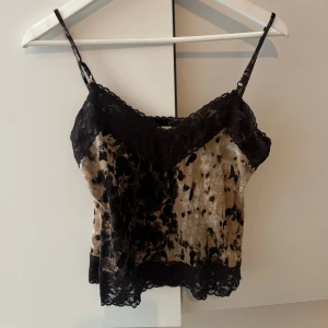 Mönstrad linne med spetsdetaljer - Snygg linne med smala axelband och spetsdetaljer. Mönstret är i svart och beige med en unik design. Perfekt för en trendig look.