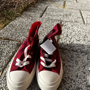 Röda sneakers med mönster all stars converse  - Snygga röda sneakers med ett unikt mönster och vita snören. Skorna har en klassisk design med vit tåhätta och sula. Perfekta för att ge din stil en färgklick.
