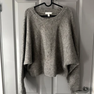 Grå stickad tröja från H&M - Mysig grå stickad tröja från H&M med en avslappnad passform. Tröjan har långa ärmar och ribbade kanter vid hals, ärmslut och nederkant. 