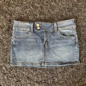 Jeanskjol med knappar - Snygg jeanskjol i klassisk blå denim med två dekorativa knappar framtill. Kjolen har både fram- och bakfickor. Står storlek 38 men passar mer än XS/S
